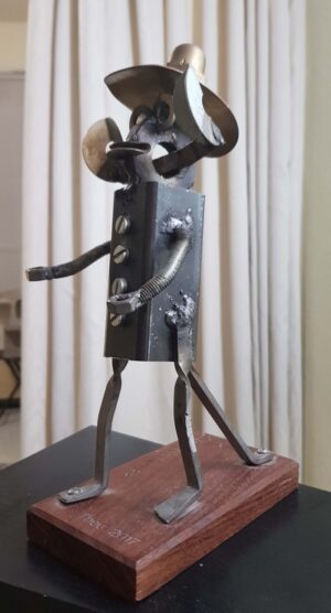 Gepuntlast metalen beeldje met grote uitstaande oren en een sombrero van gebogen, koperen gasbuis op her hoofd getiteld: "Hoort u mij."